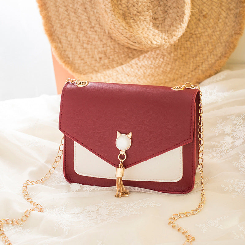 Red handbag with gold chain and cat design on a white surface with a straw hat in the background