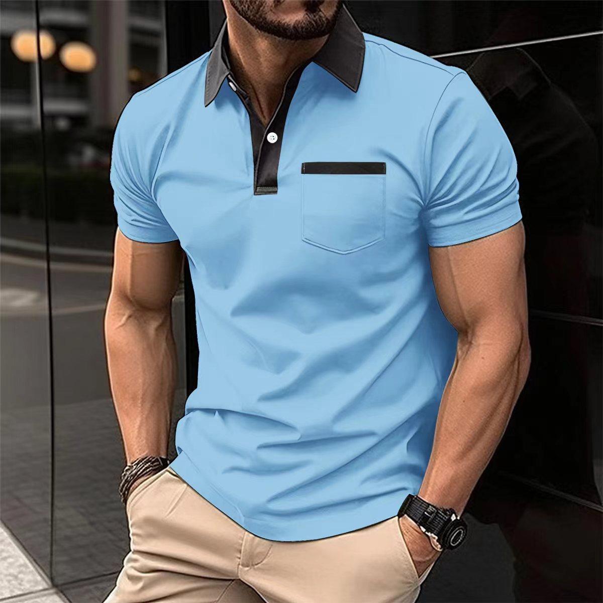 Man wearing a light blue polo shirt with black collar and pocket, standing against a reflective surface.