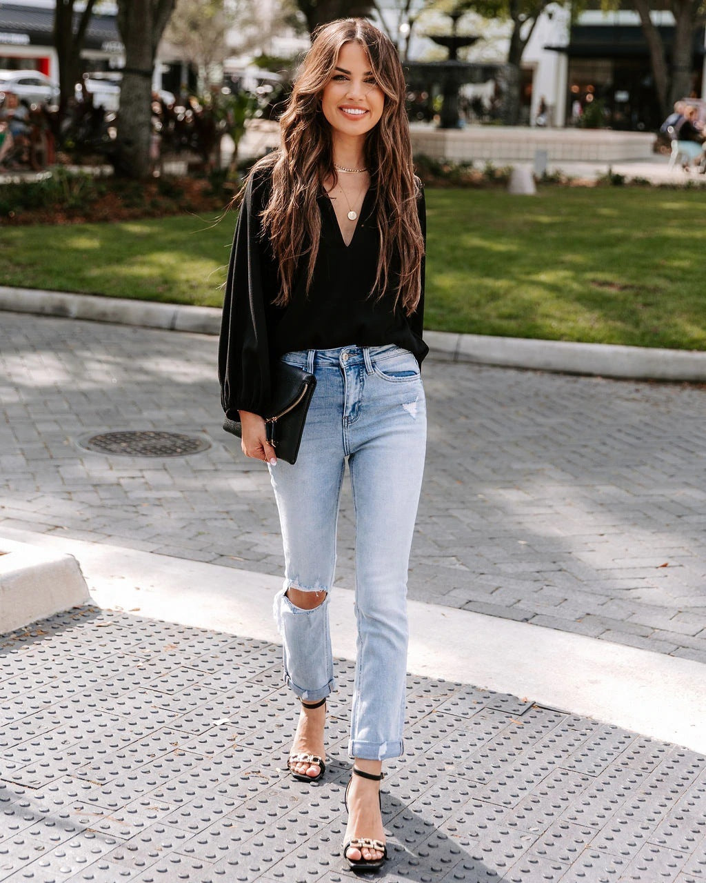 Woman wearing a black top and light blue jeans on a city street.