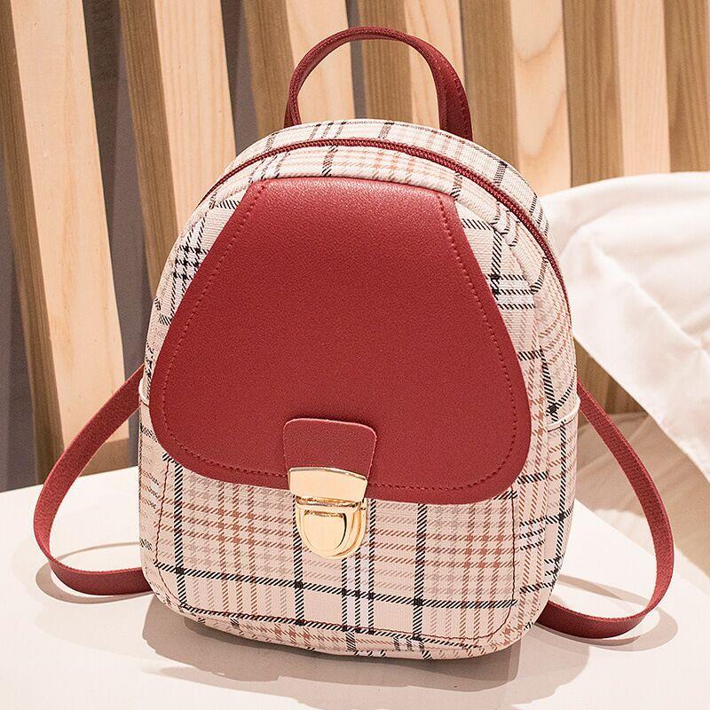 Small backpack with plaid pattern and red front section on a light wooden surface.