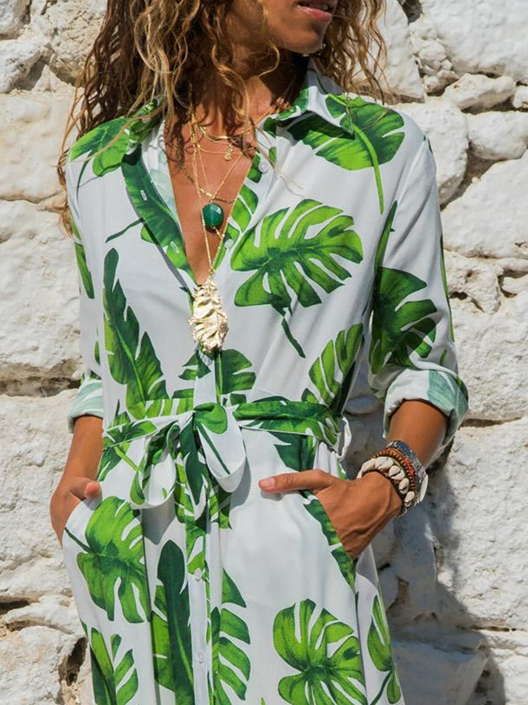 Woman wearing a tropical leaf print dress against a stone wall.