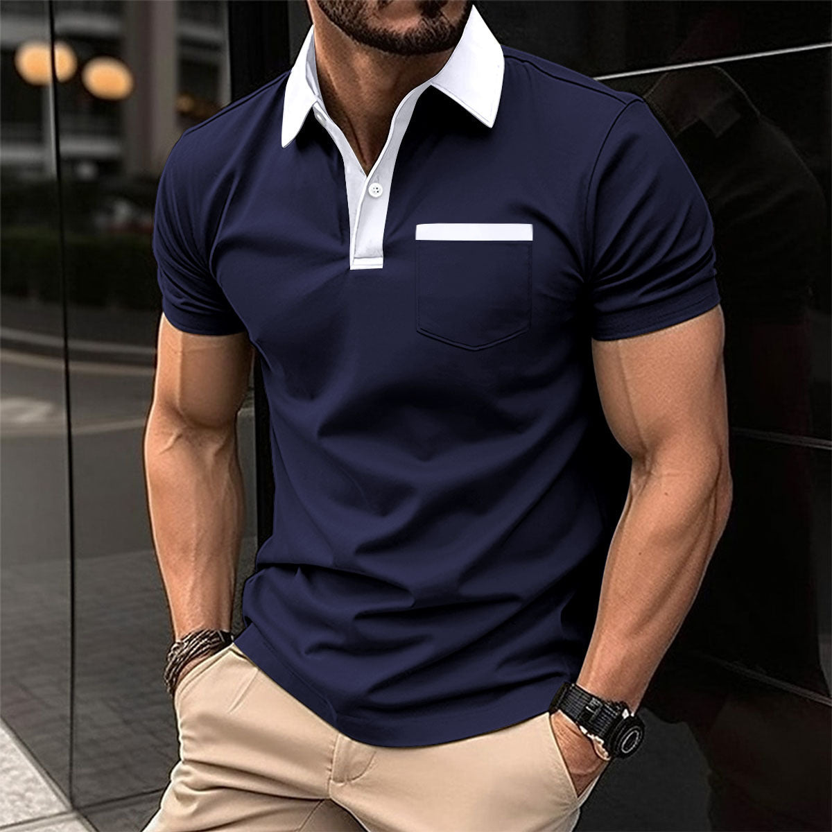 Man wearing a navy blue polo shirt with a white collar and beige pants, standing against a reflective surface.
