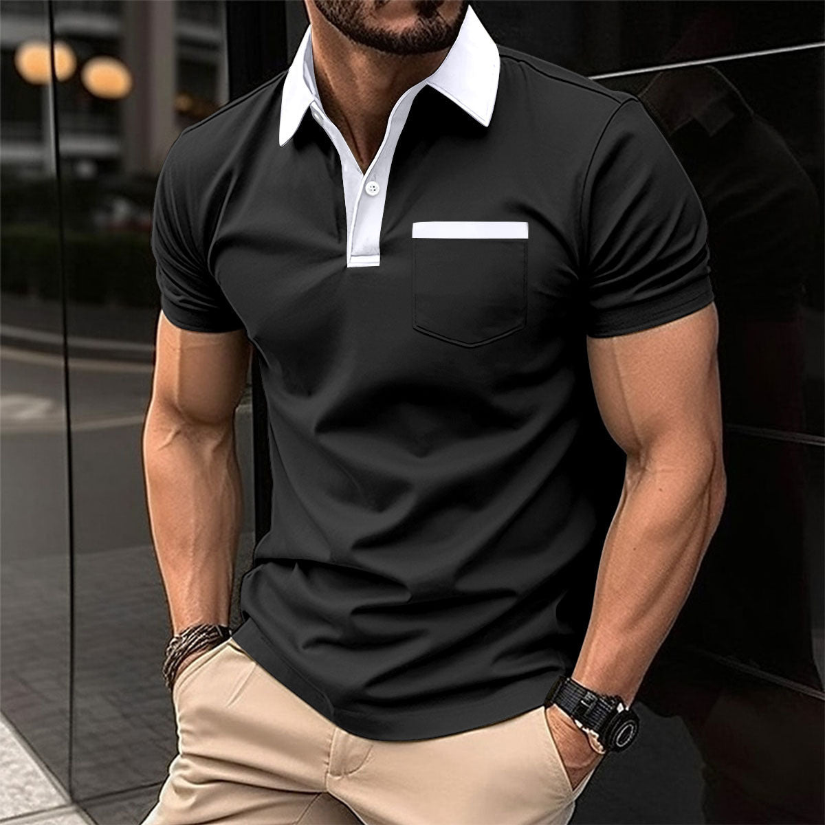 Man wearing a black polo shirt with a white collar and beige pants, standing against a reflective surface.