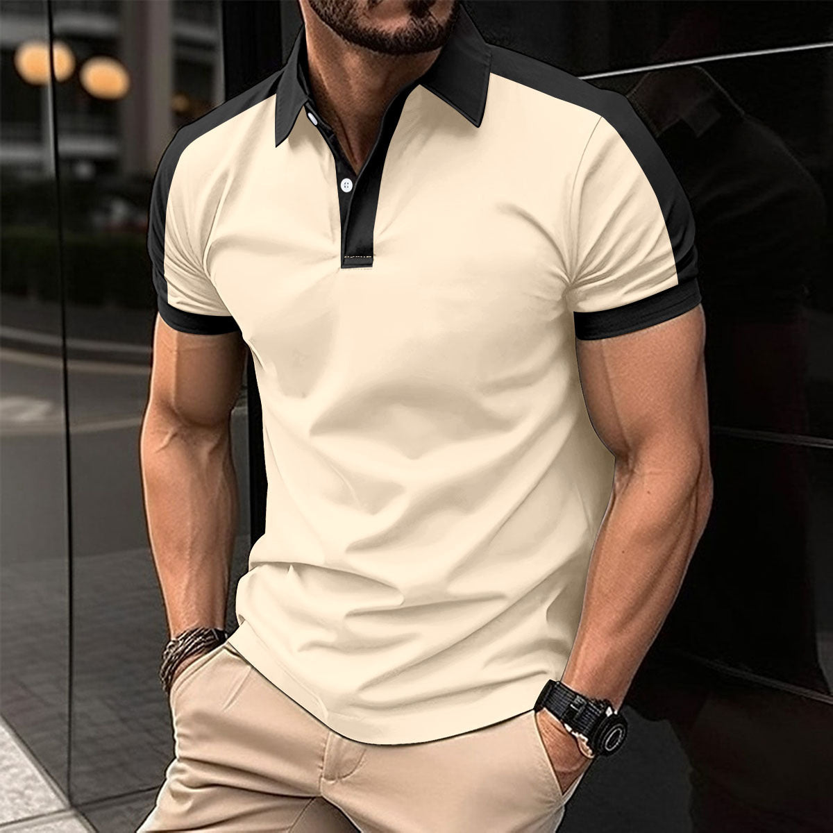 Man wearing a beige and black polo shirt with beige pants, standing against a blurred background.
