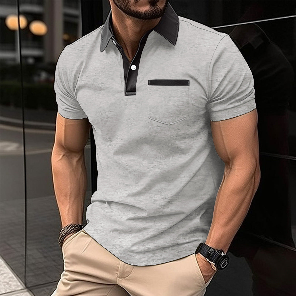 Man wearing a gray polo shirt with black collar and pocket trim, standing against a blurred background.