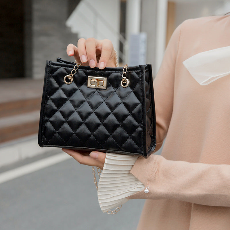 Person holding a black quilted handbag with gold accents.