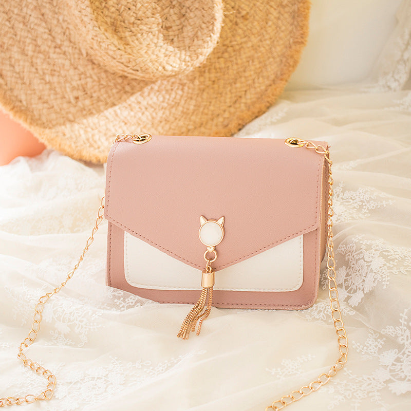 Pink handbag with gold chain and tassel on a soft white background