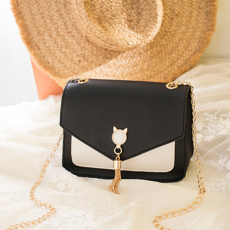 Black handbag with gold chain and cat-shaped charm on a soft white background