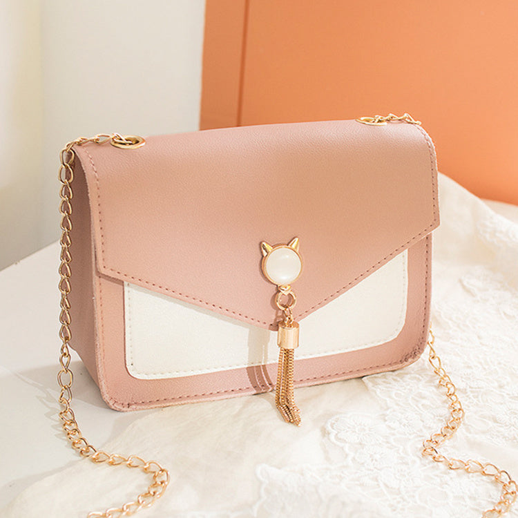 Pink handbag with gold chain and cat-shaped charm on a white surface.