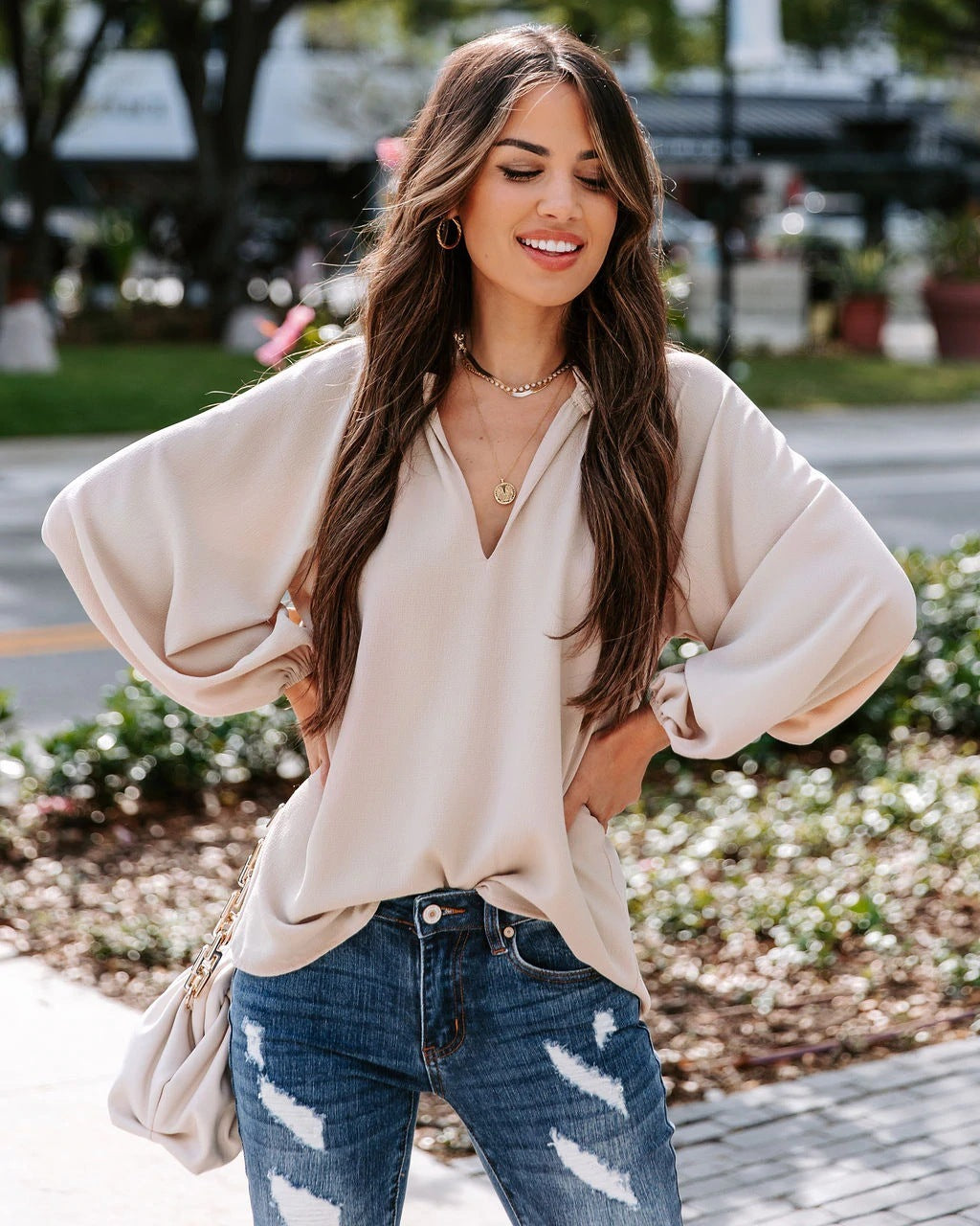 Woman wearing a beige blouse and blue jeans outdoors