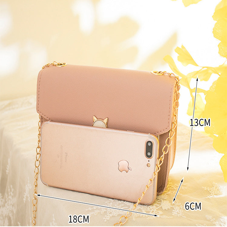 Beige handbag with chain strap and smartphone inside, on a light yellow background