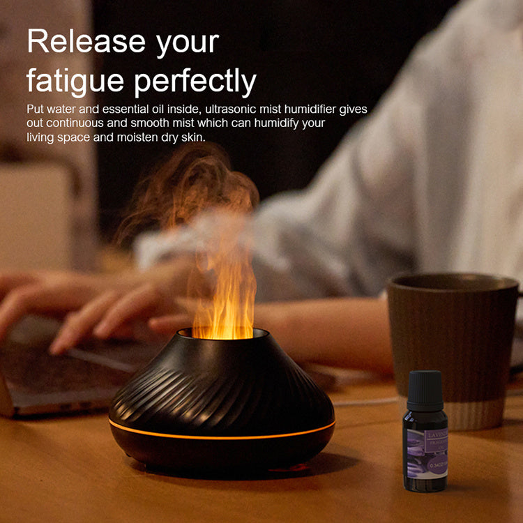 Ultrasonic mist humidifier with essential oil bottle on a table, person using laptop in the background.