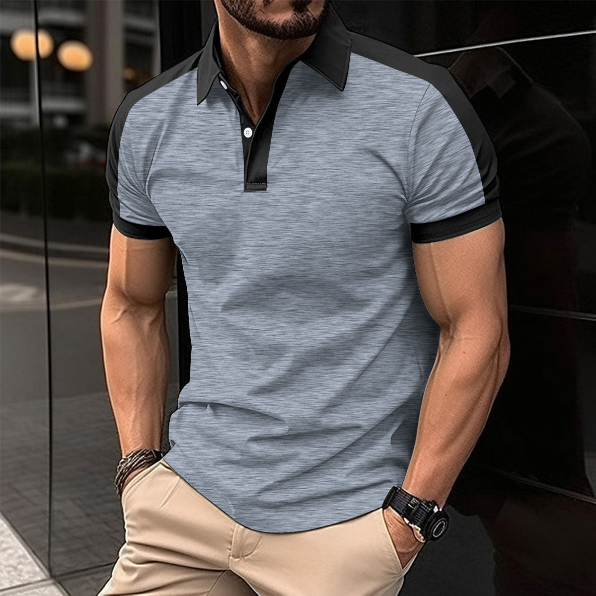 Man wearing a gray polo shirt with black accents and beige pants, standing against a blurred background.