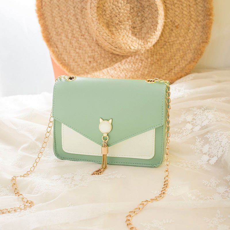 Mint green handbag with gold chain on a soft white surface with a straw hat in the background