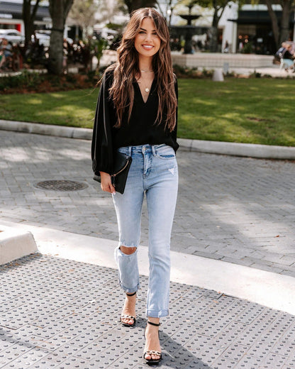 Woman wearing a black top and light blue jeans on a city street.