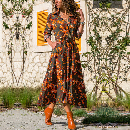 Woman wearing a floral dress and orange boots standing in front of a stone wall with plants.