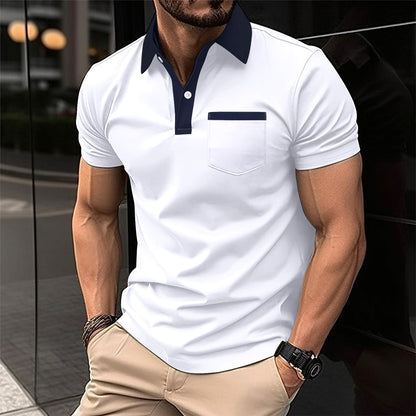 Man wearing a white polo shirt with navy accents and beige pants, standing against a reflective surface.