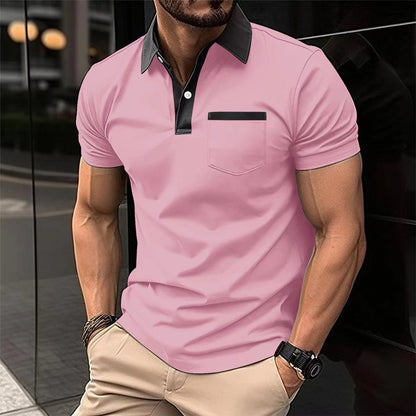 Man wearing a pink polo shirt with black collar and pocket trim, standing against a blurred background.