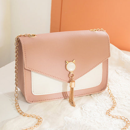 Pink handbag with gold chain and cat-shaped charm on a white surface.