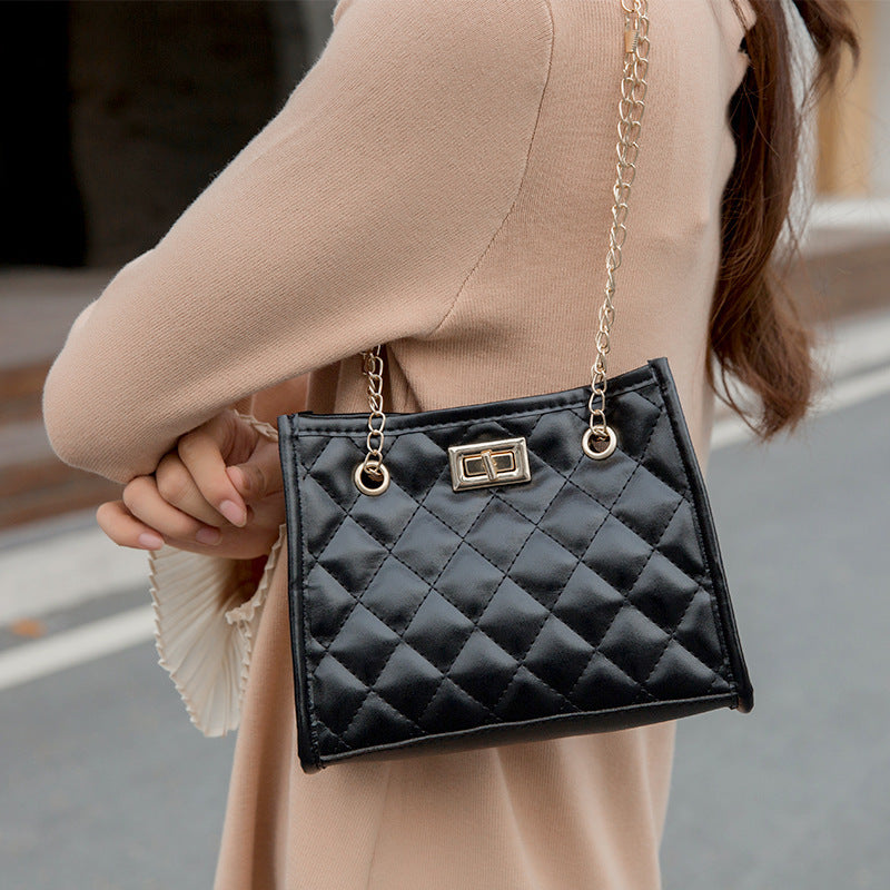 Black quilted handbag with gold chain strap held by a person wearing a beige sweater.