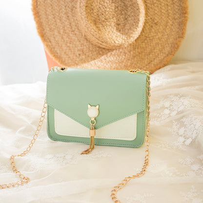 Mint green handbag with gold chain on a soft white surface with a straw hat in the background